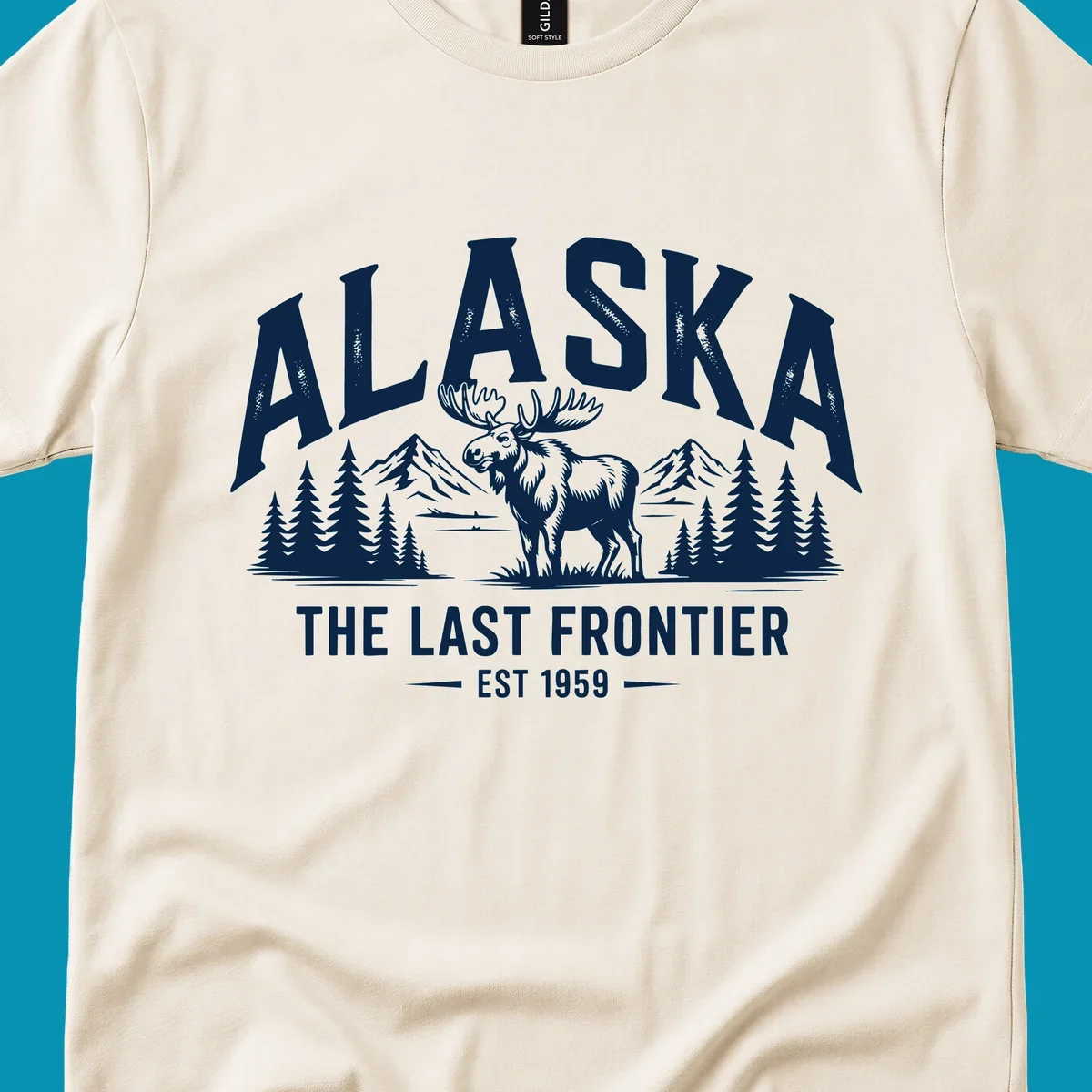A white alaska-moose-frontier-scenic graphic showing a moose standing in front of mountains and pine trees.