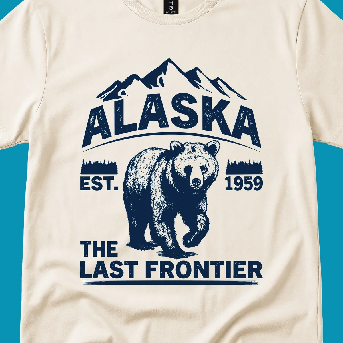 White graphic of a walking grizzly bear under mountain peaks with alaska-grizzly-frontier-mountains text.