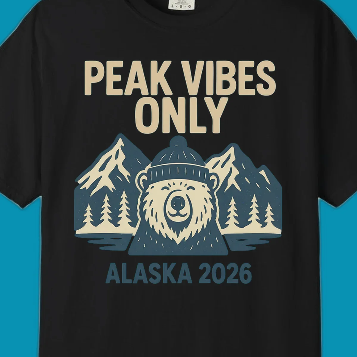 Vintage badge-style illustration of a smiling bear wearing a beanie with snow-capped mountains, evergreen trees, and water, text reads Peak Vibes Only Alaska 2026