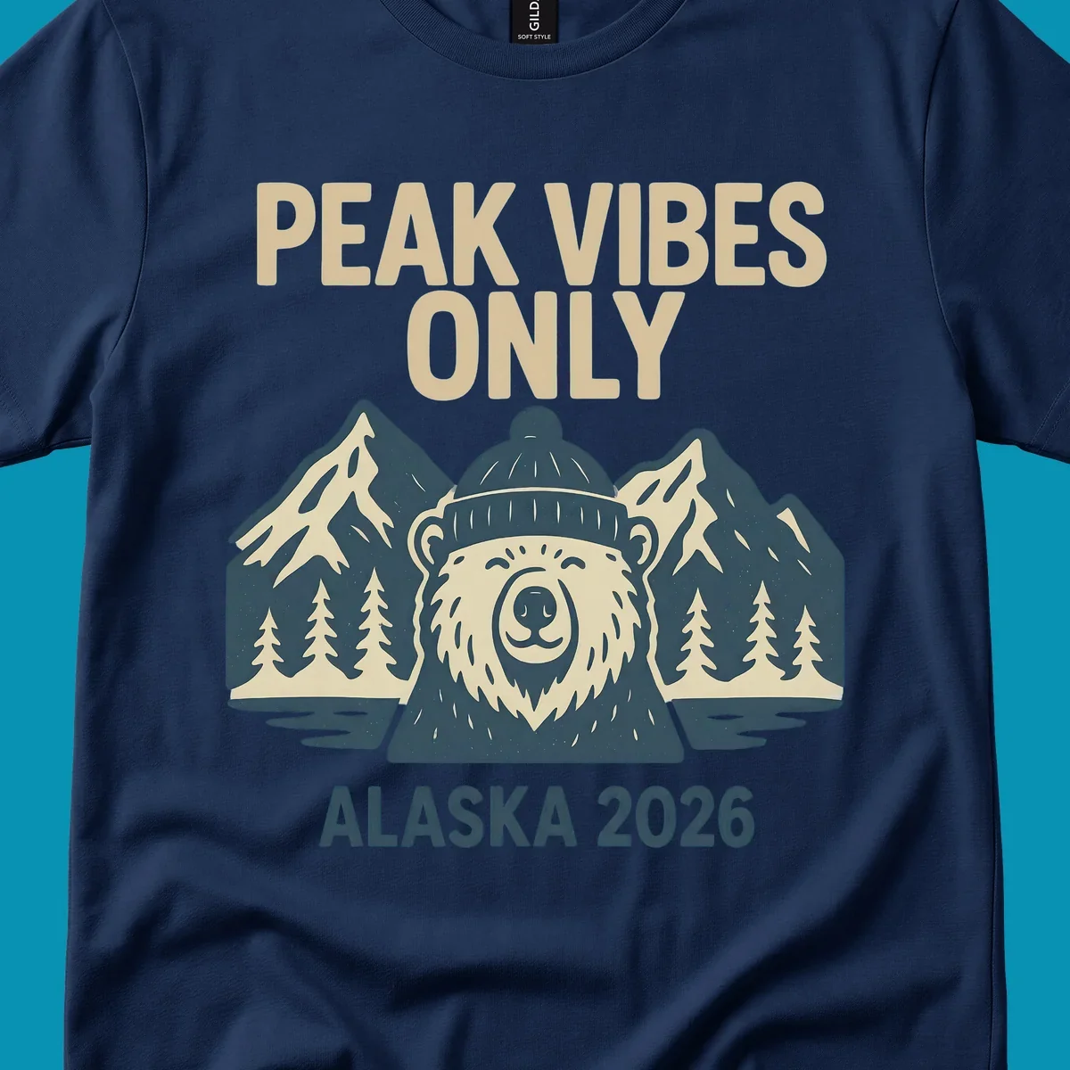 Vintage badge-style illustration of a smiling bear wearing a beanie with snow-capped mountains, evergreen trees, and water, text reads Peak Vibes Only Alaska 2026