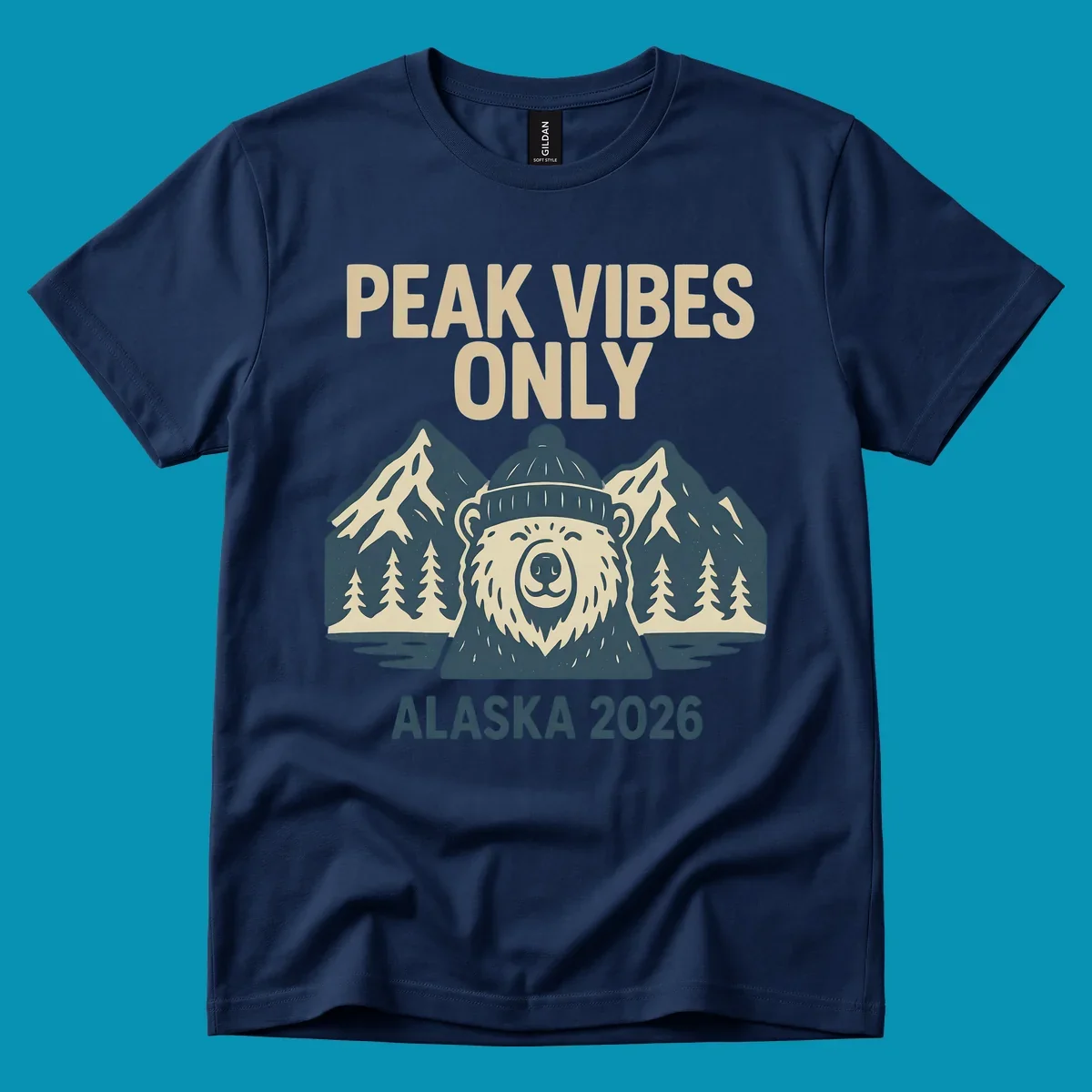 Vintage badge-style illustration of a smiling bear wearing a beanie with snow-capped mountains, evergreen trees, and water, text reads Peak Vibes Only Alaska 2026
