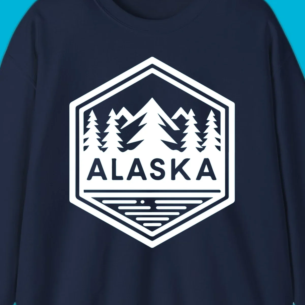 An Alaska mountain lake badge design in a hexagon shape, showing mountains, pine trees, and a lake below the ALASKA text.