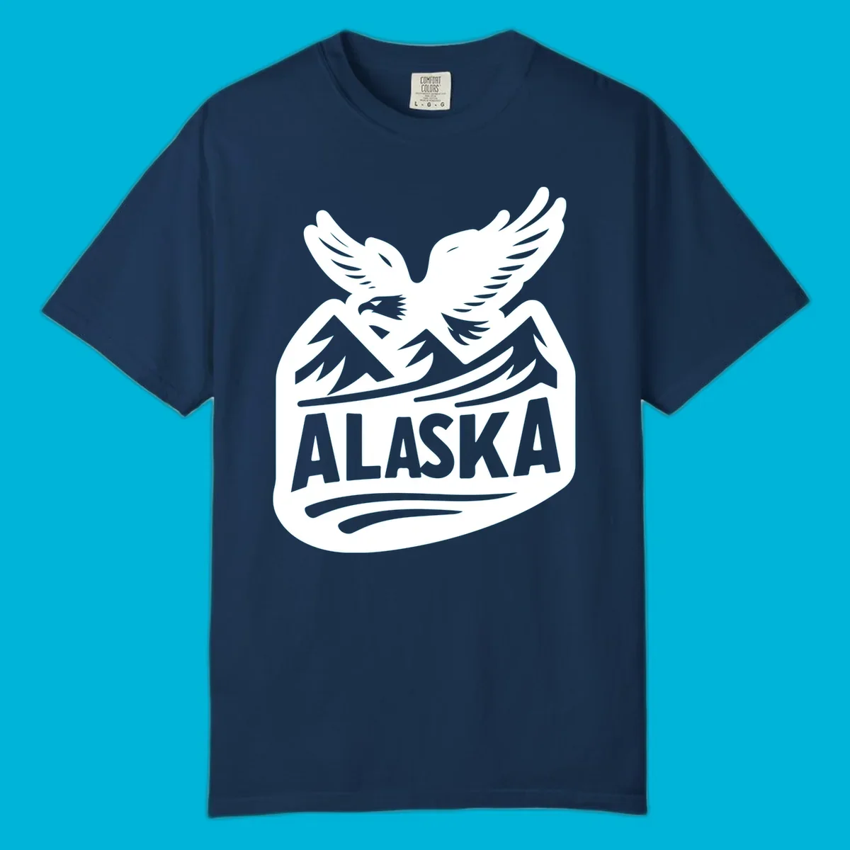 A white and dark blue badge design showing a flying eagle over mountain peaks with "ALASKA" text, for a cruise souvenir.