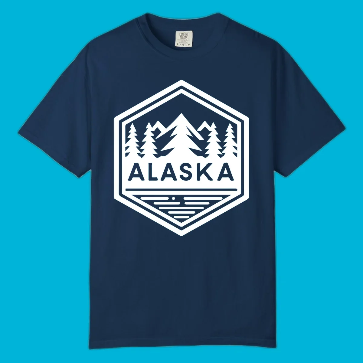 An Alaska mountain lake badge design in a hexagon shape, showing mountains, pine trees, and a lake below the ALASKA text.