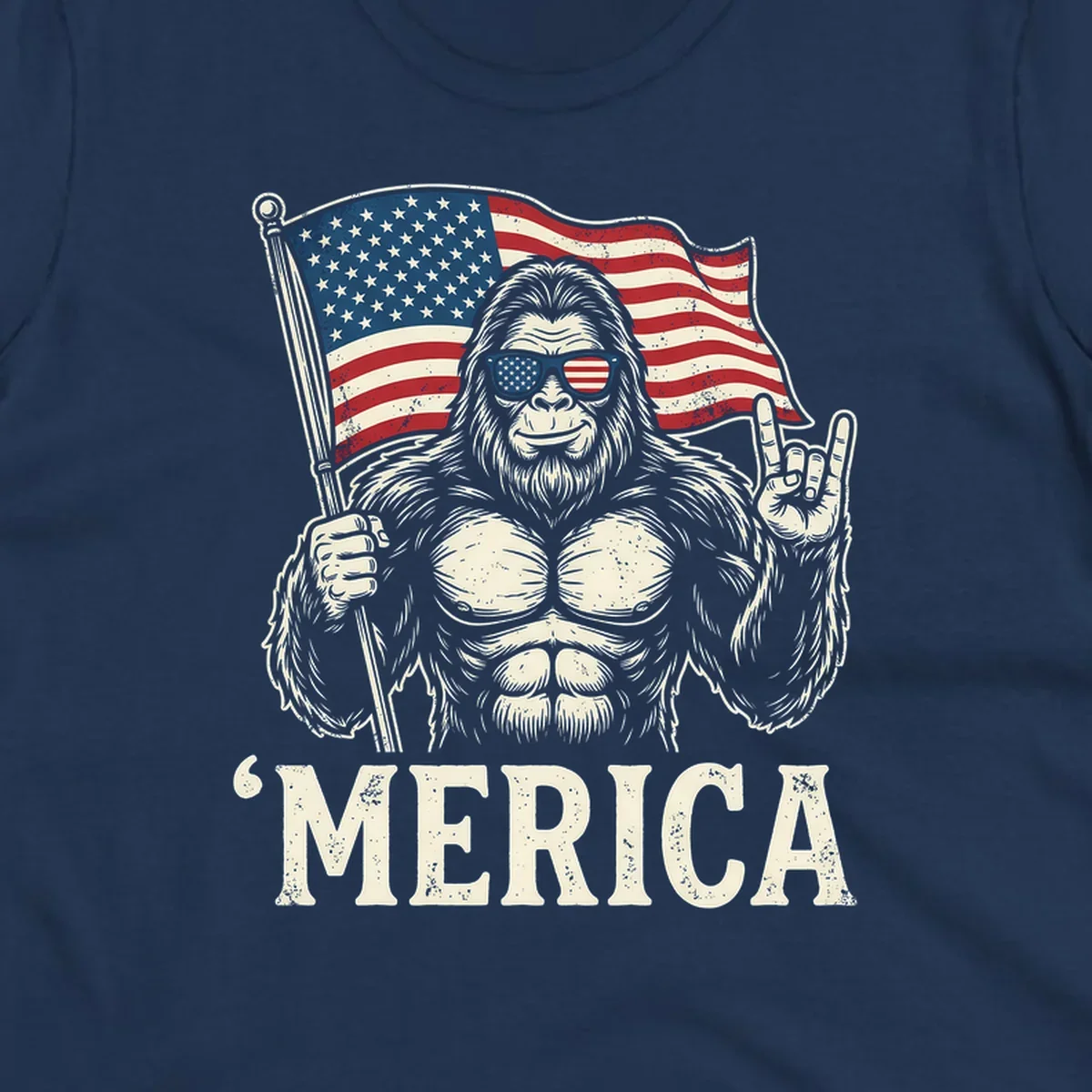 A muscular Bigfoot with American flag sunglasses holds a flag and makes a rock on sign, with "'MERICA" text, for a patriotic Bigfoot 'Merica tee.
