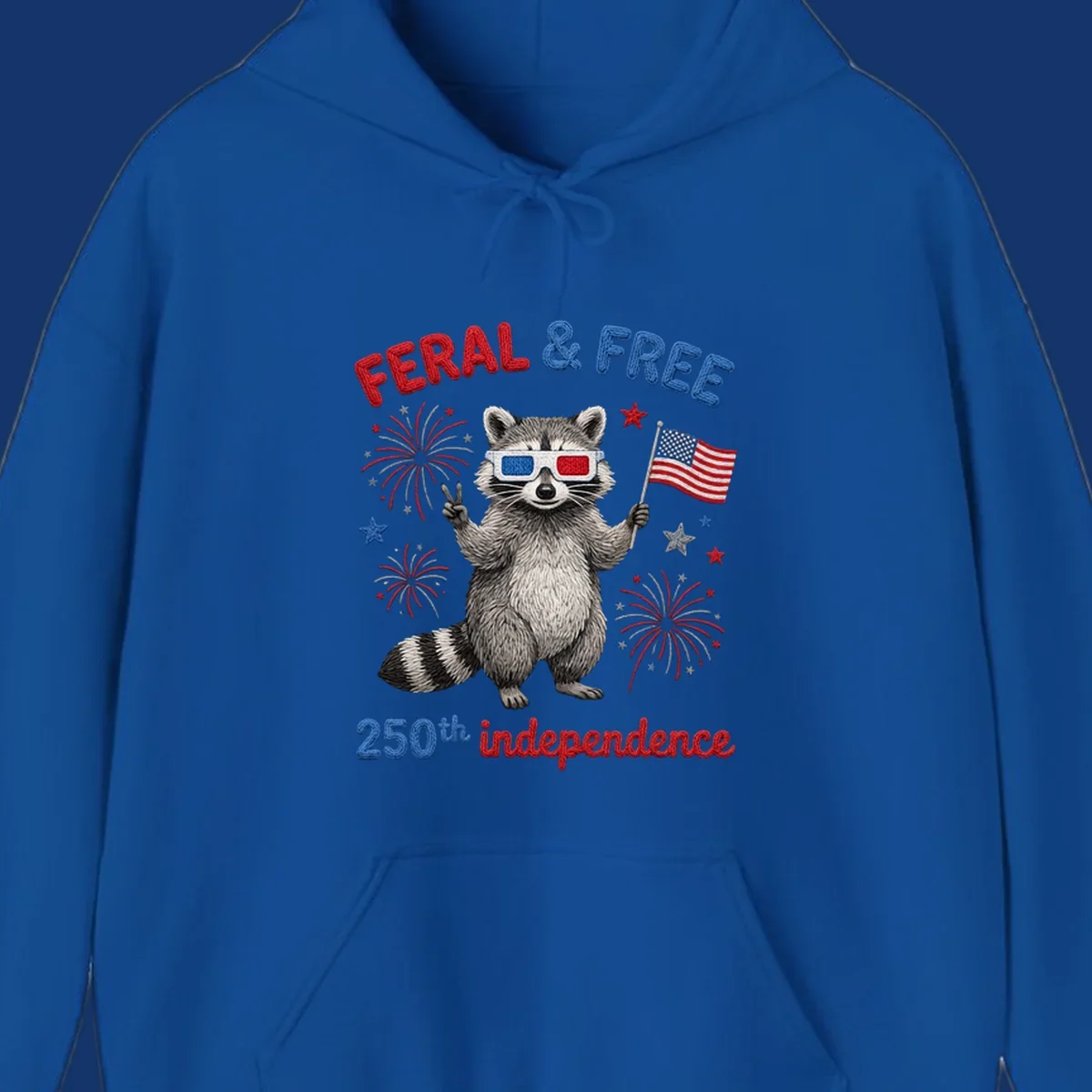 A "FERAL & FREE" raccoon in 3D glasses holds an American flag, surrounded by fireworks, celebrating 250th independence.