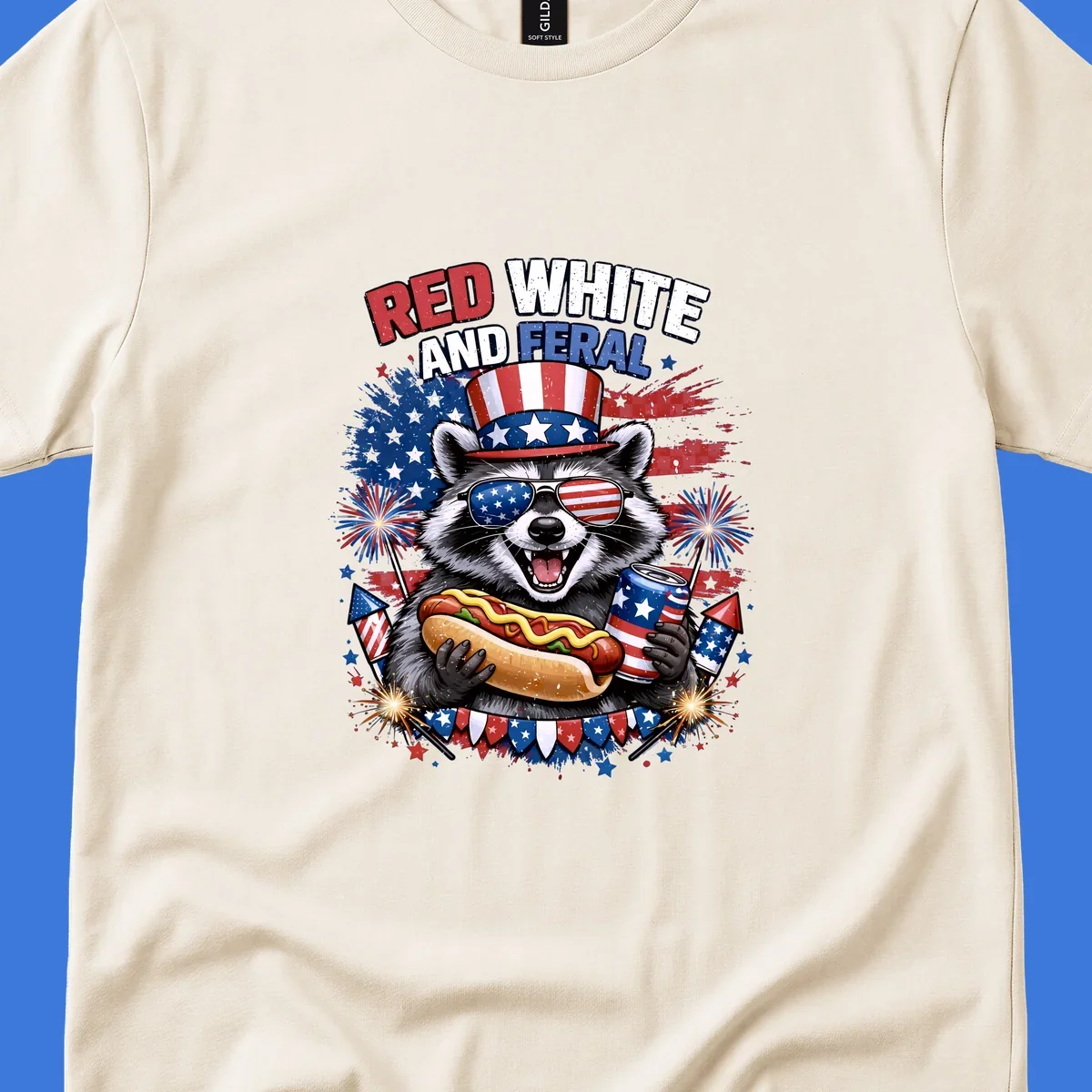 A patriotic raccoon wearing an American flag top hat and sunglasses, holding a hot dog and soda can, with the text 'RED WHITE AND FERAL' and fireworks.