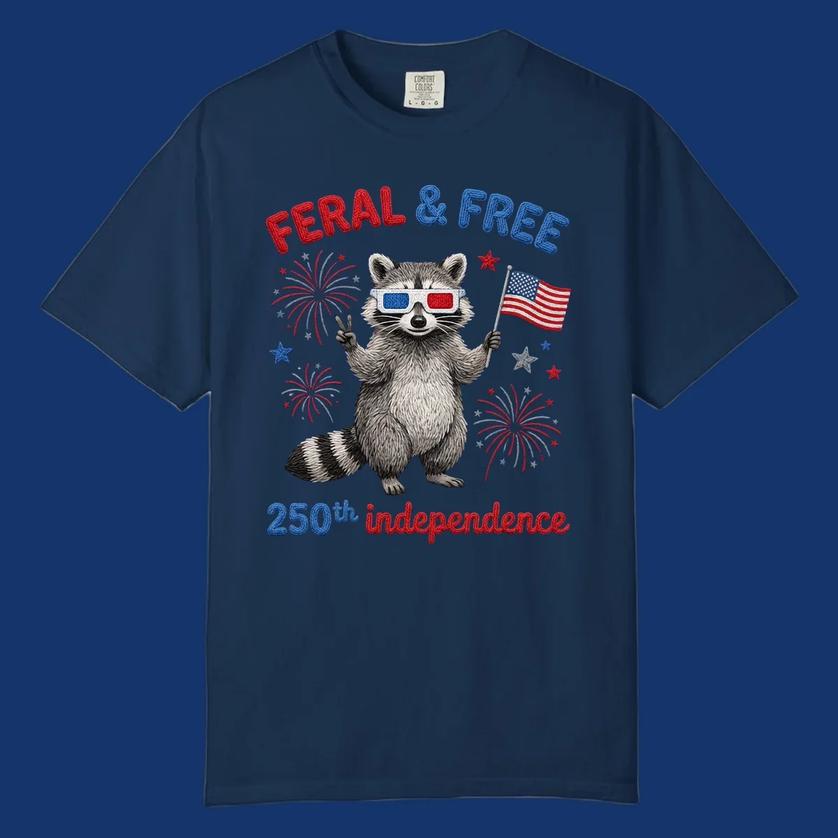 A playful raccoon in 3D glasses holds an American flag, surrounded by fireworks and stars, with "FERAL & FREE 250th independence".