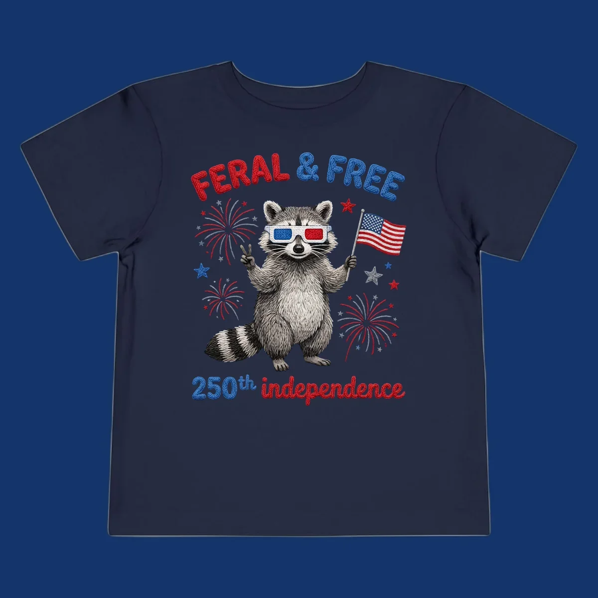 A playful raccoon in 3D glasses holds an American flag, surrounded by fireworks and stars, with "FERAL & FREE 250th independence".