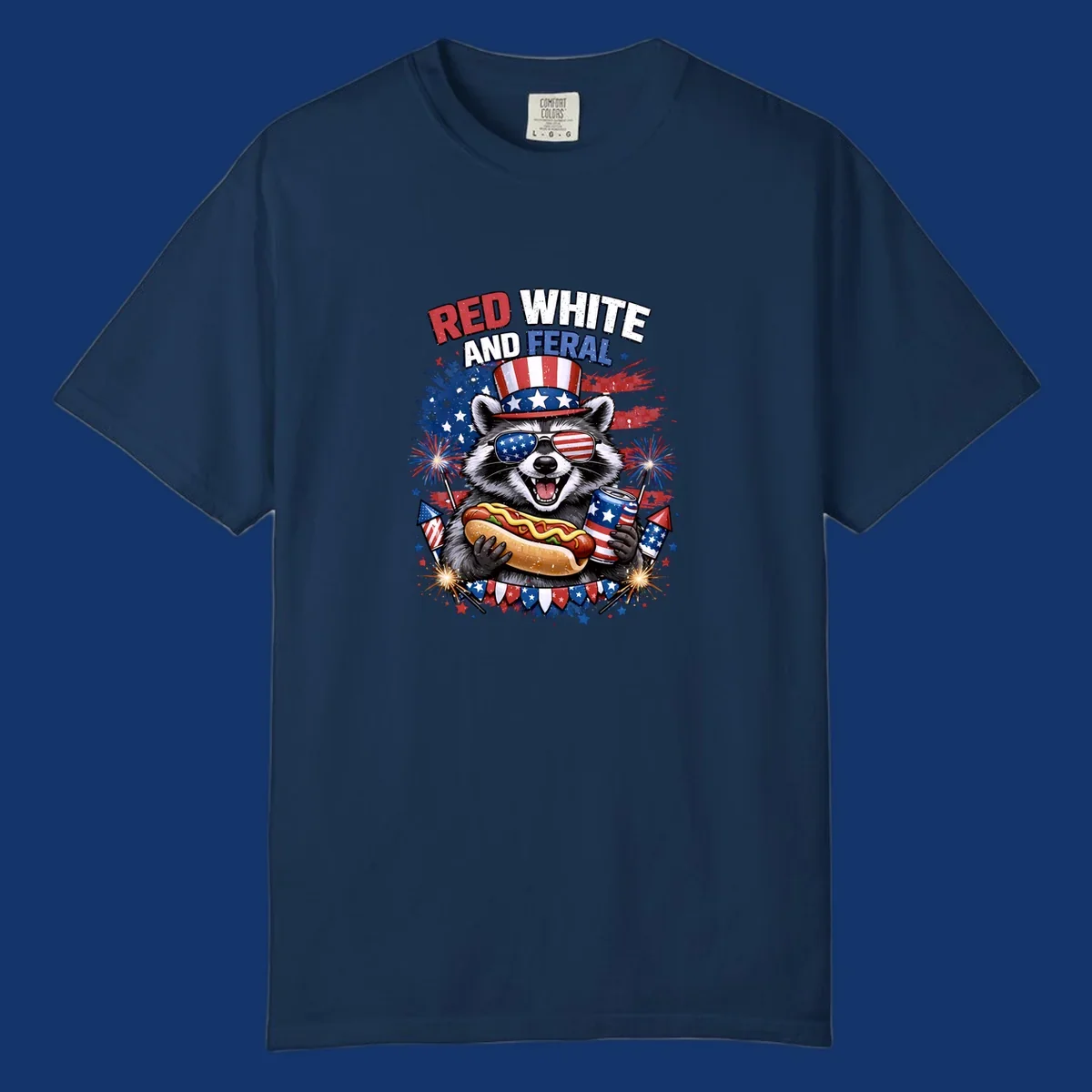 A patriotic raccoon wearing an American flag top hat and sunglasses, holding a hot dog and soda can, with the text 'RED WHITE AND FERAL' and fireworks.