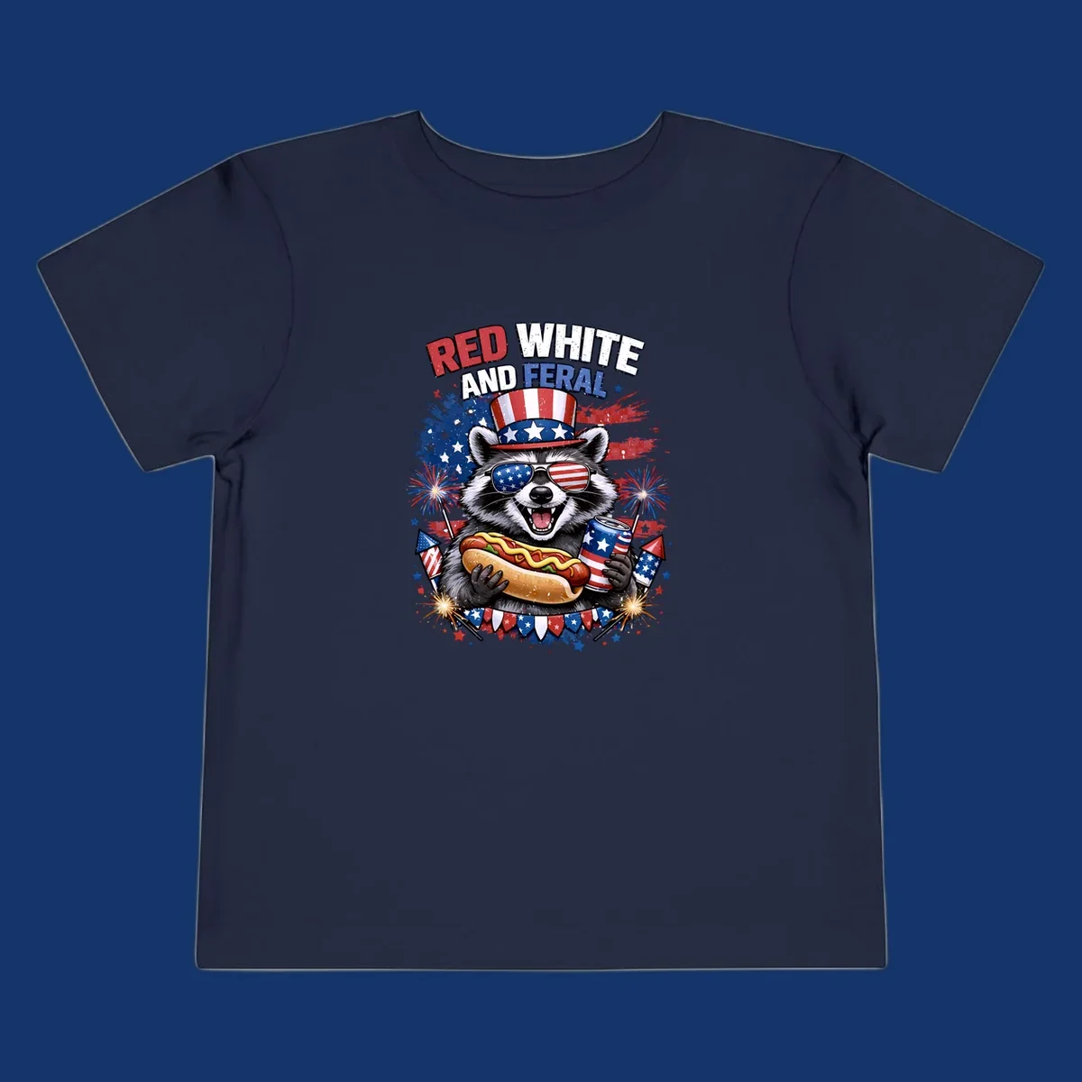 A patriotic raccoon wearing an American flag top hat and sunglasses, holding a hot dog and soda can, with the text 'RED WHITE AND FERAL' and fireworks.