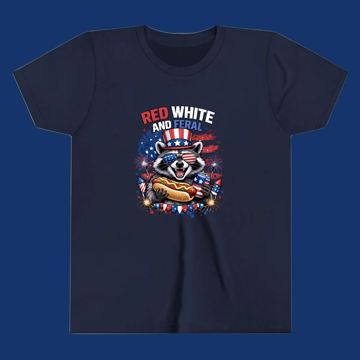 A patriotic raccoon wearing an American flag top hat and sunglasses, holding a hot dog and soda can, with the text 'RED WHITE AND FERAL' and fireworks.