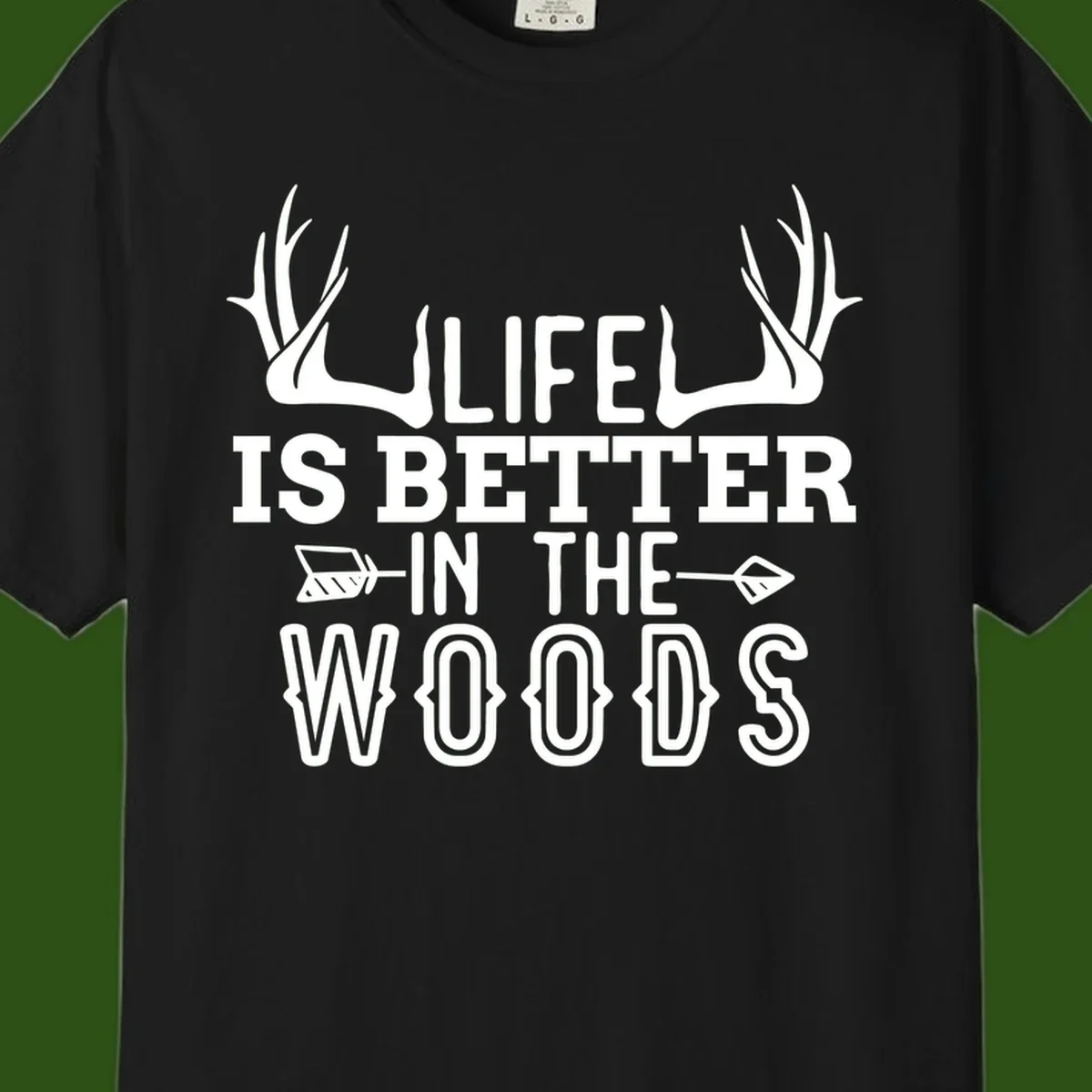 White text reading 'Life Is Better In The Woods' with deer antlers and arrows on gray background