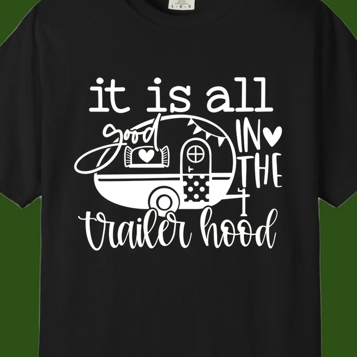 Vintage trailer illustration with decorative hearts and bunting, text reading 'it is all good in the trailer hood' in retro style