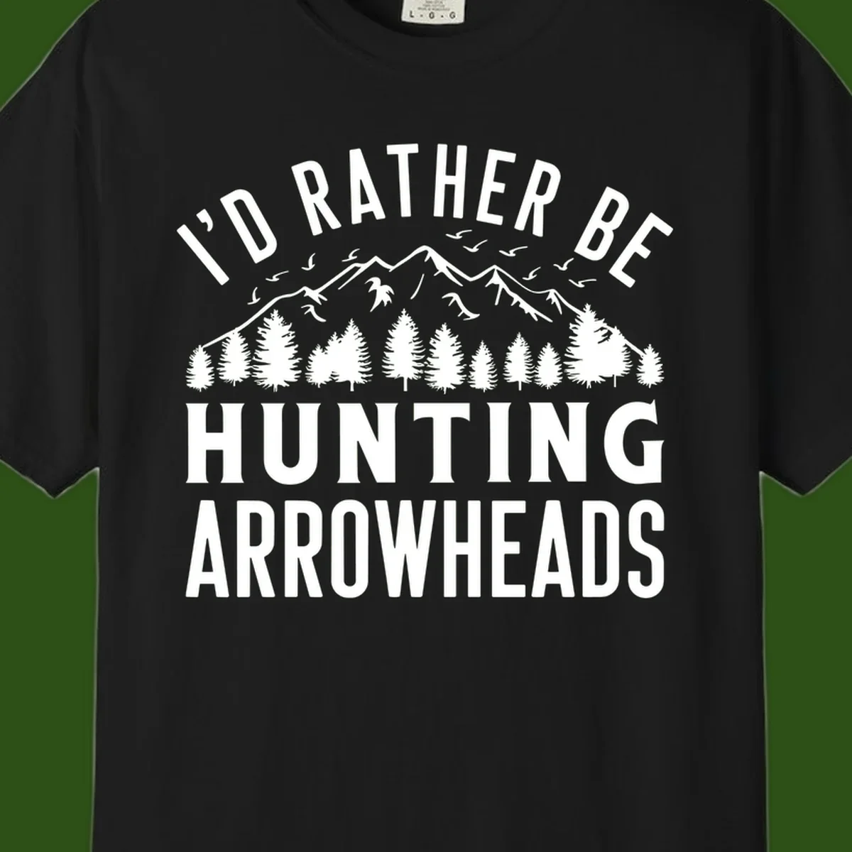 Mountain landscape with evergreen trees and birds, white text reading 'I'd Rather Be Hunting Arrowheads' on gray background