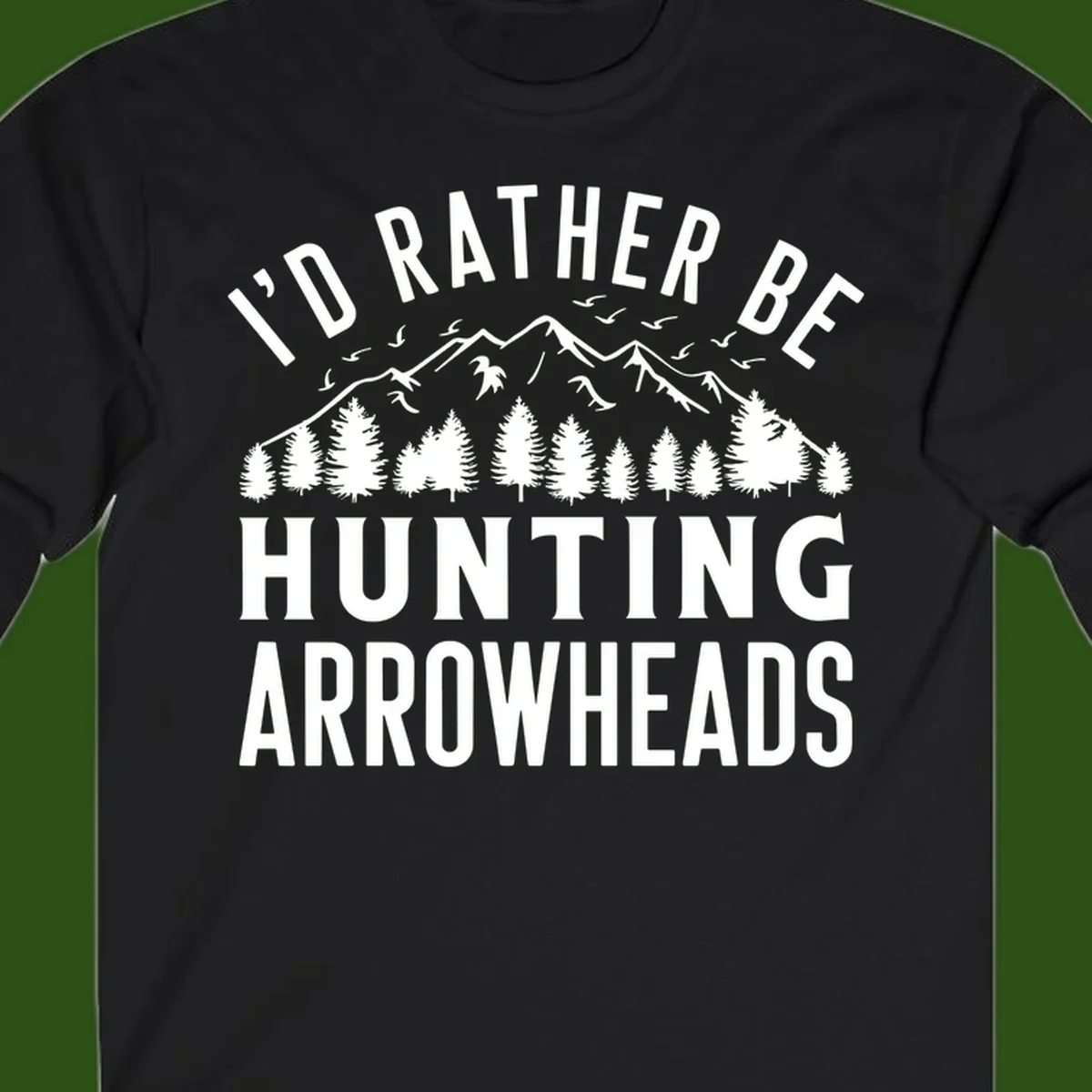 Mountain landscape with evergreen trees and birds, white text reading 'I'd Rather Be Hunting Arrowheads' on gray background