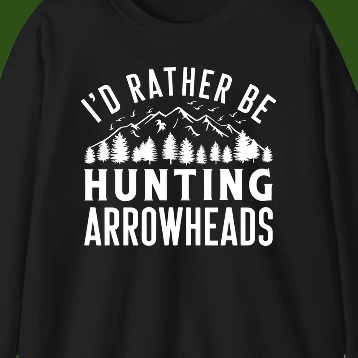 Mountain landscape with evergreen trees and birds, white text reading 'I'd Rather Be Hunting Arrowheads' on gray background