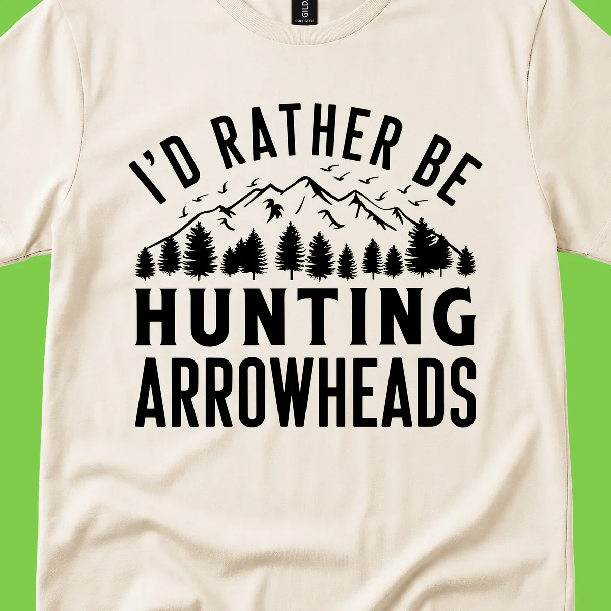 Mountain landscape with evergreen trees and birds, white text reading 'I'd Rather Be Hunting Arrowheads' on gray background