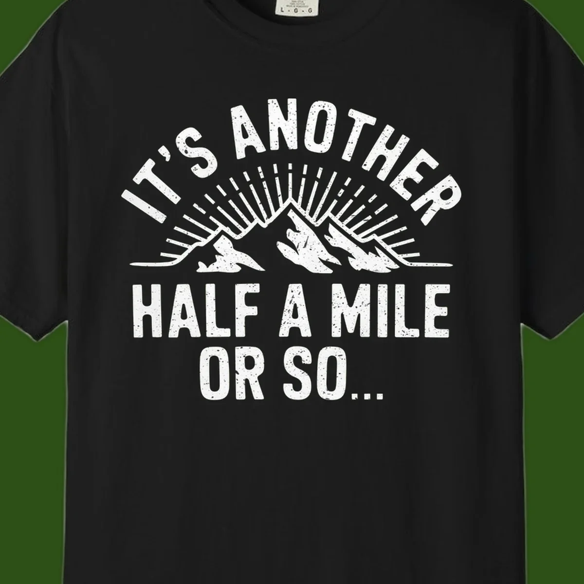 Retro distressed design with mountain peaks and sun rays, text reads 'It's Another Half A Mile Or So' - humorous hiking and camping artwork