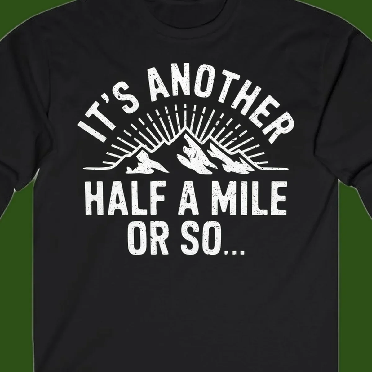 Retro distressed design with mountain peaks and sun rays, text reads 'It's Another Half A Mile Or So' - humorous hiking and camping artwork