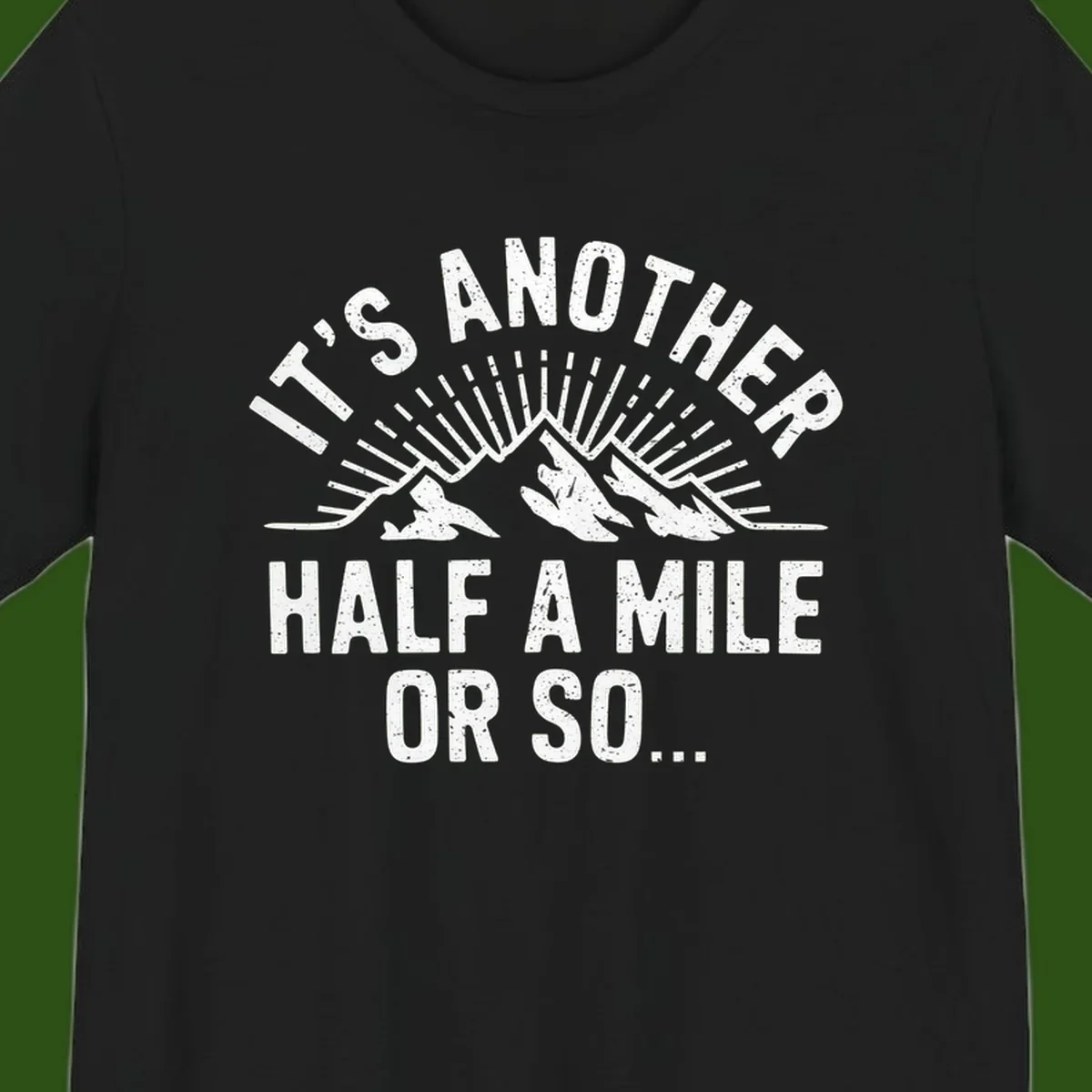 Retro distressed design with mountain peaks and sun rays, text reads 'It's Another Half A Mile Or So' - humorous hiking and camping artwork
