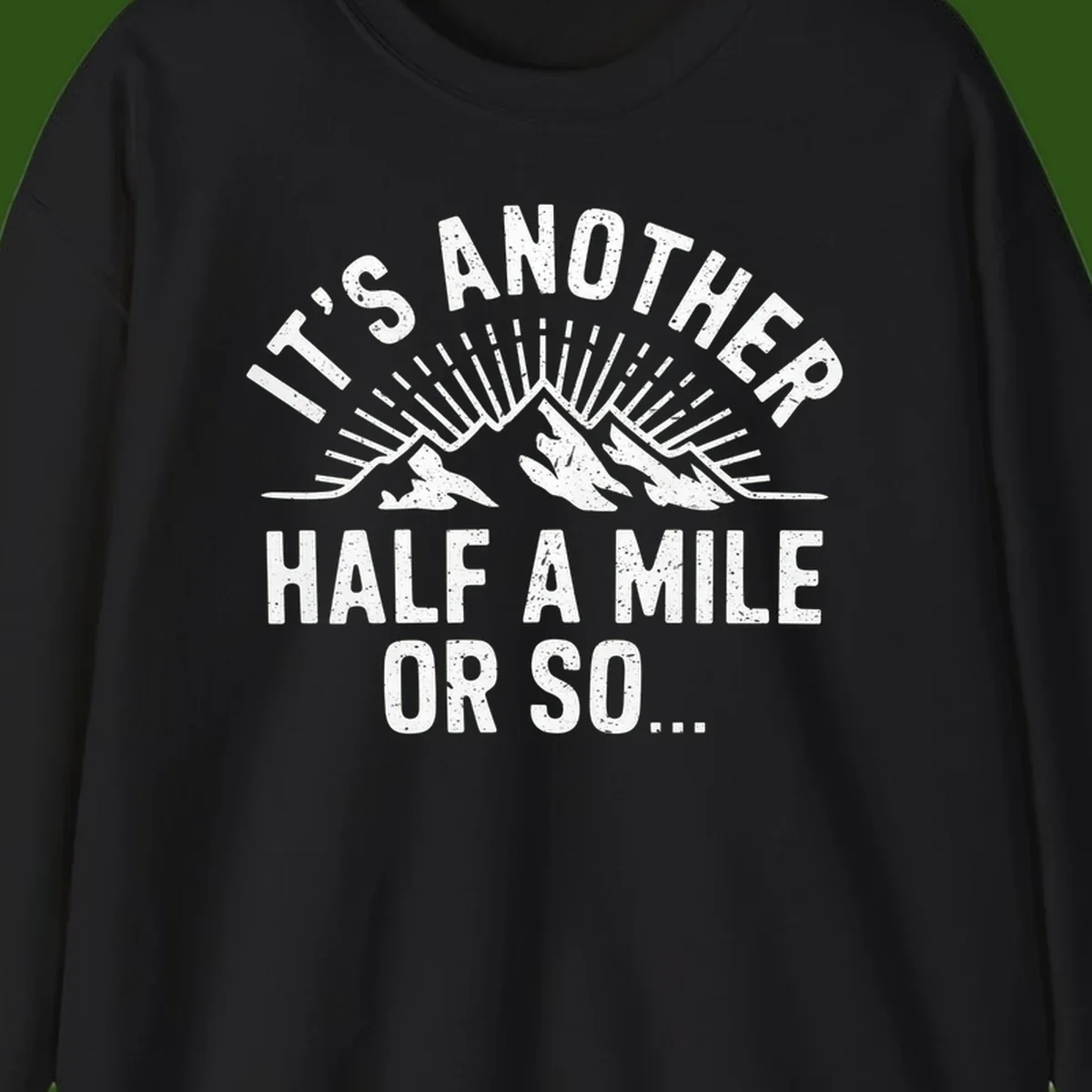 Retro distressed design with mountain peaks and sun rays, text reads 'It's Another Half A Mile Or So' - humorous hiking and camping artwork