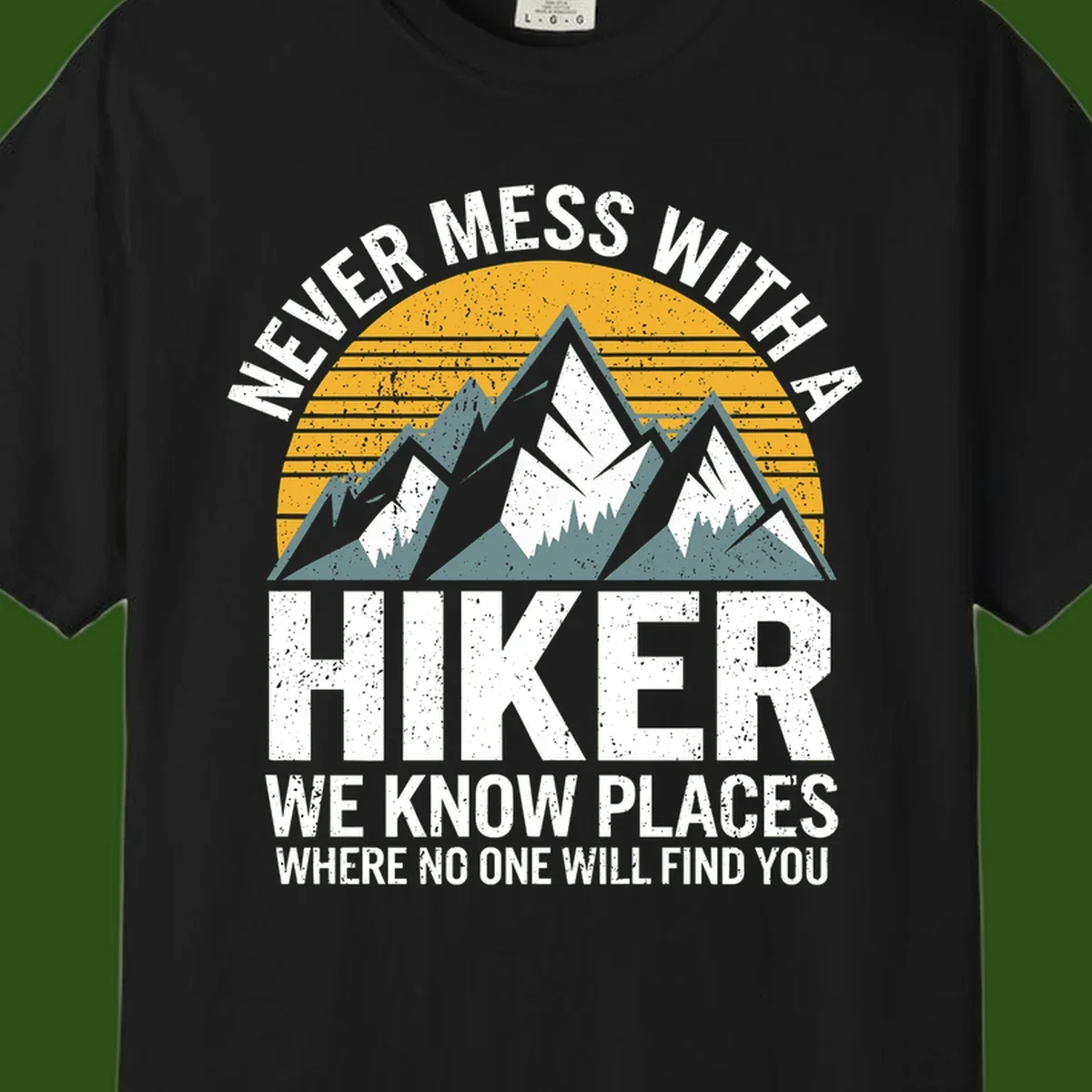 Vintage-style design with snow-capped mountains and forest silhouette against striped sunset, text reads 'Never Mess With A Hiker We Know Places Where No One Will Find You'
