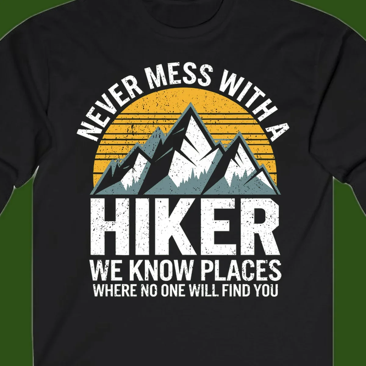 Vintage-style design with snow-capped mountains and forest silhouette against striped sunset, text reads 'Never Mess With A Hiker We Know Places Where No One Will Find You'
