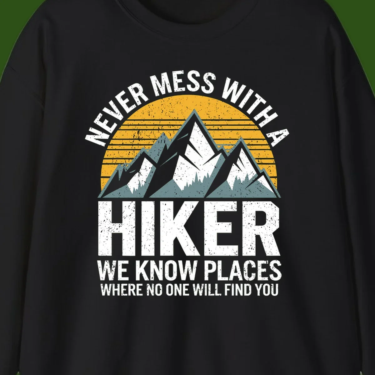 Vintage-style design with snow-capped mountains and forest silhouette against striped sunset, text reads 'Never Mess With A Hiker We Know Places Where No One Will Find You'