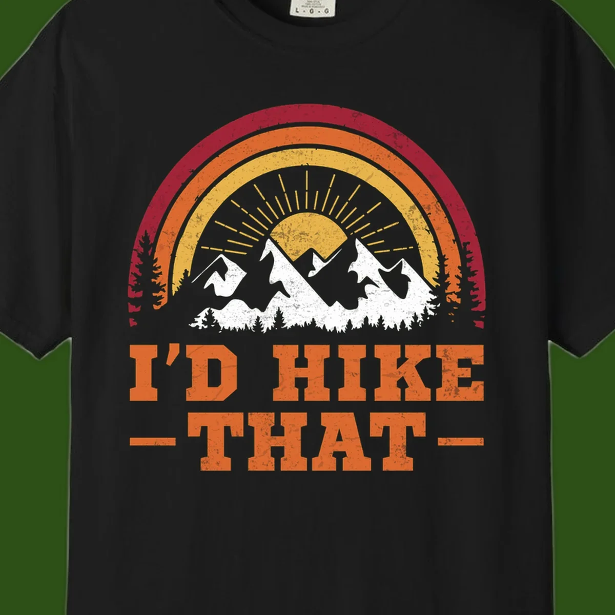 Vintage badge design with snow-capped mountains, evergreen trees, golden sun rays, and text reading 'I'd Hike That' in retro style