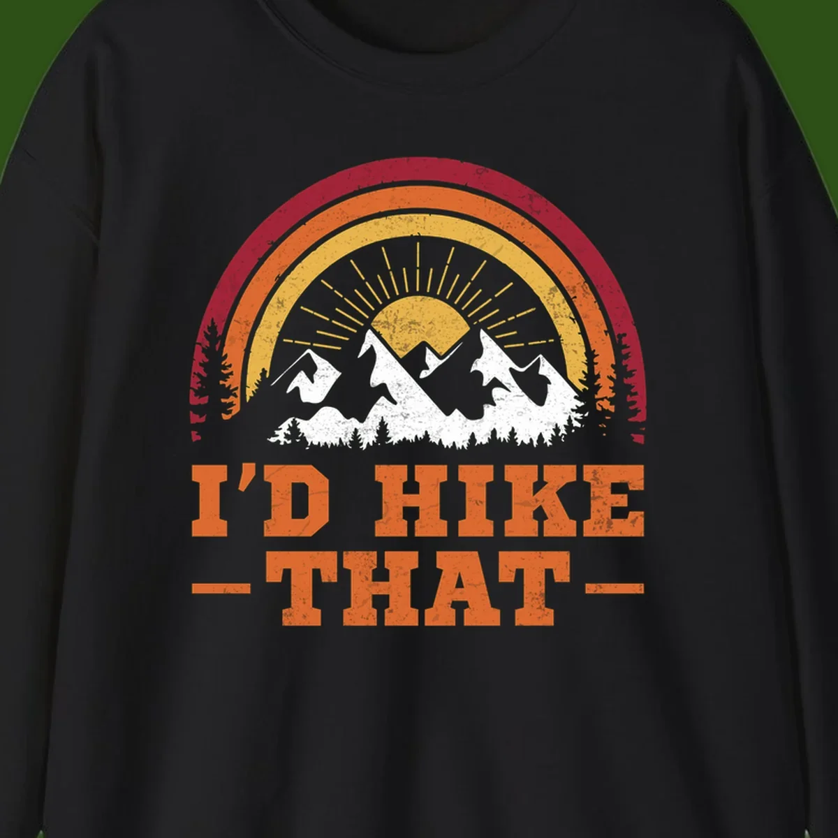 Vintage badge design with snow-capped mountains, evergreen trees, golden sun rays, and text reading 'I'd Hike That' in retro style