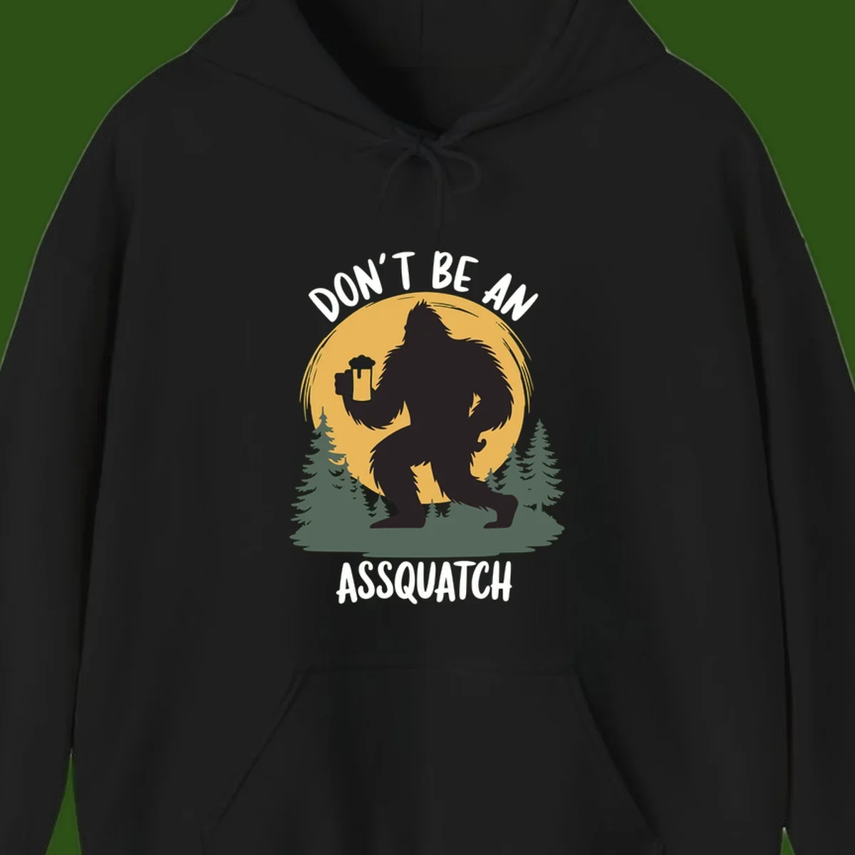 Black silhouette of Bigfoot holding a beer mug under a full moon with pine trees, text reads don't be an assquatch