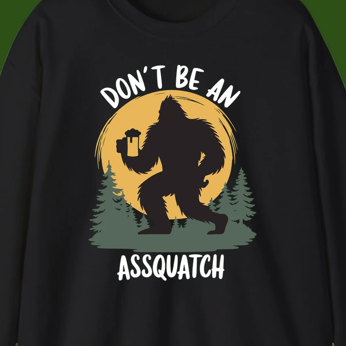 Black silhouette of Bigfoot holding a beer mug under a full moon with pine trees, text reads don't be an assquatch
