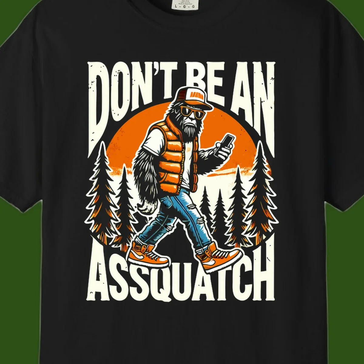 Cartoon sasquatch in hiking gear with backpack and smartphone, 'Don't Be An Assquatch' text, forest and orange sun background.