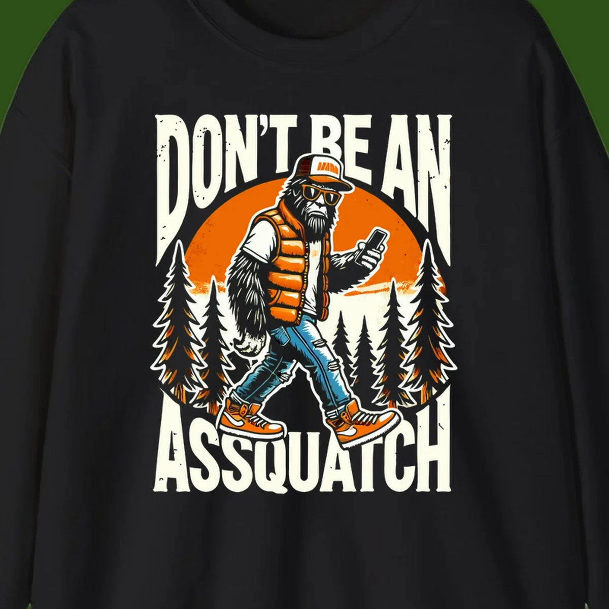 Cartoon sasquatch in hiking gear with backpack and smartphone, 'Don't Be An Assquatch' text, forest and orange sun background.
