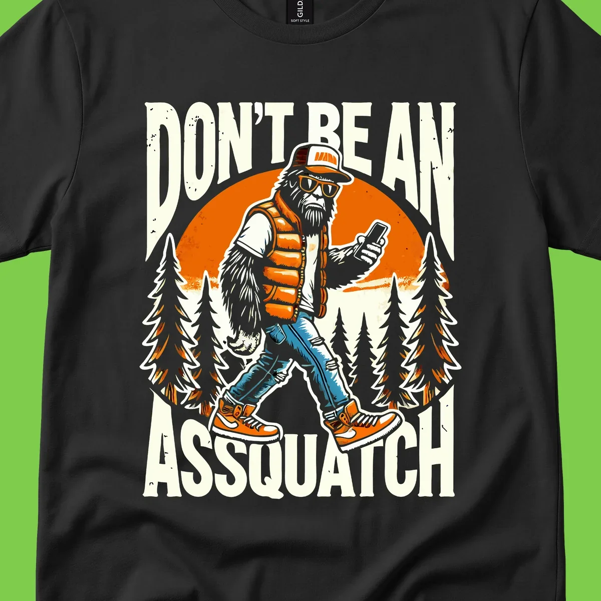 Cartoon sasquatch in hiking gear with backpack and smartphone, 'Don't Be An Assquatch' text, forest and orange sun background.