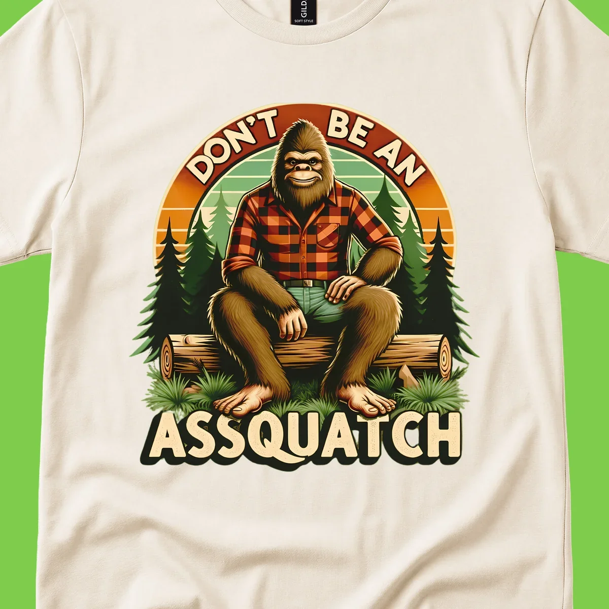 Vintage badge design with friendly Bigfoot in plaid shirt sitting on a log with forest trees, text reads 'Don't Be An Assquatch'
