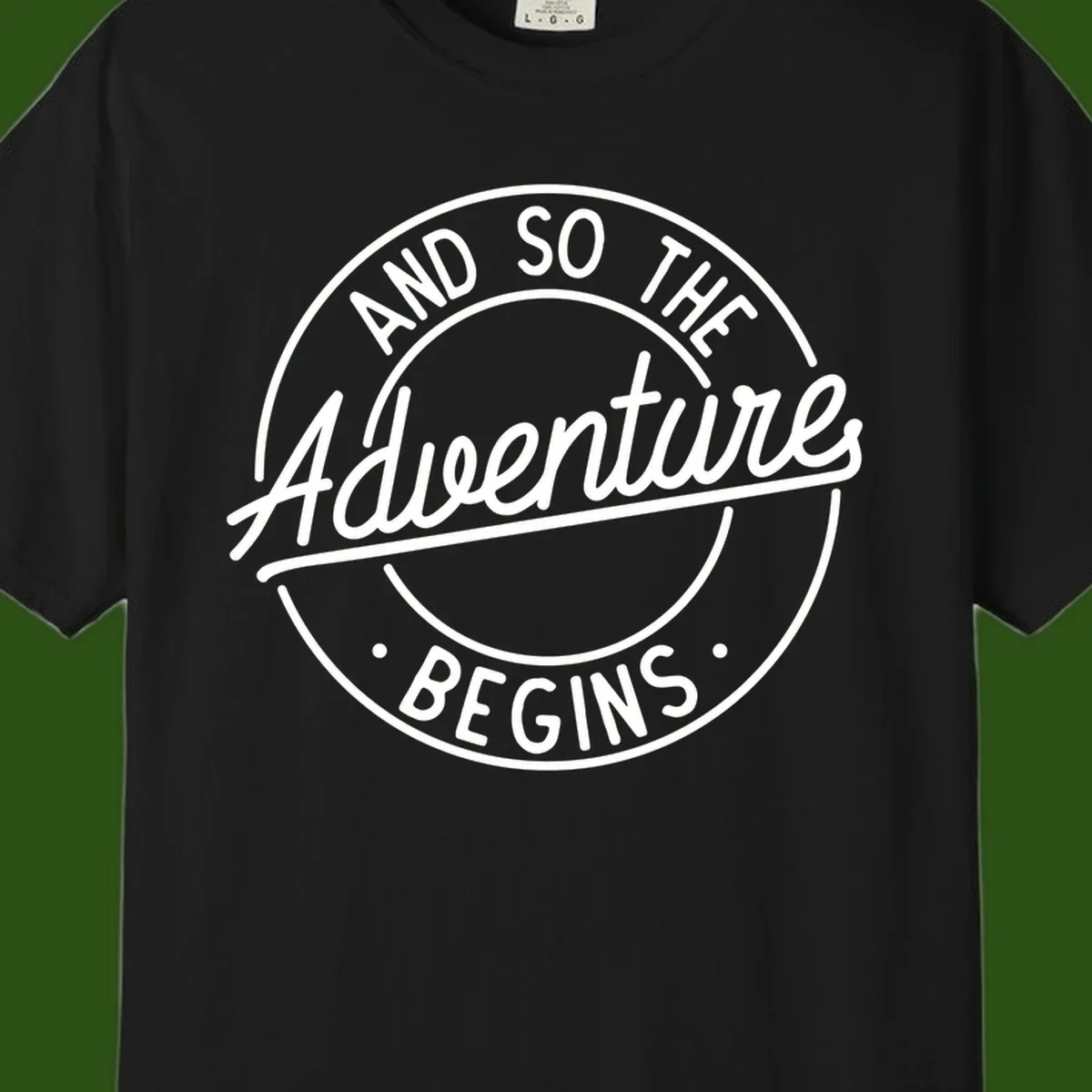 Vintage circular badge design with white text reading 'And So The Adventure Begins' on gray background