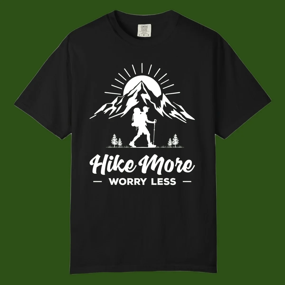 Silhouette of hiker with backpack and poles facing snow-capped mountain with radiating sun, evergreen trees below, text reads 'Hike More Worry Less'