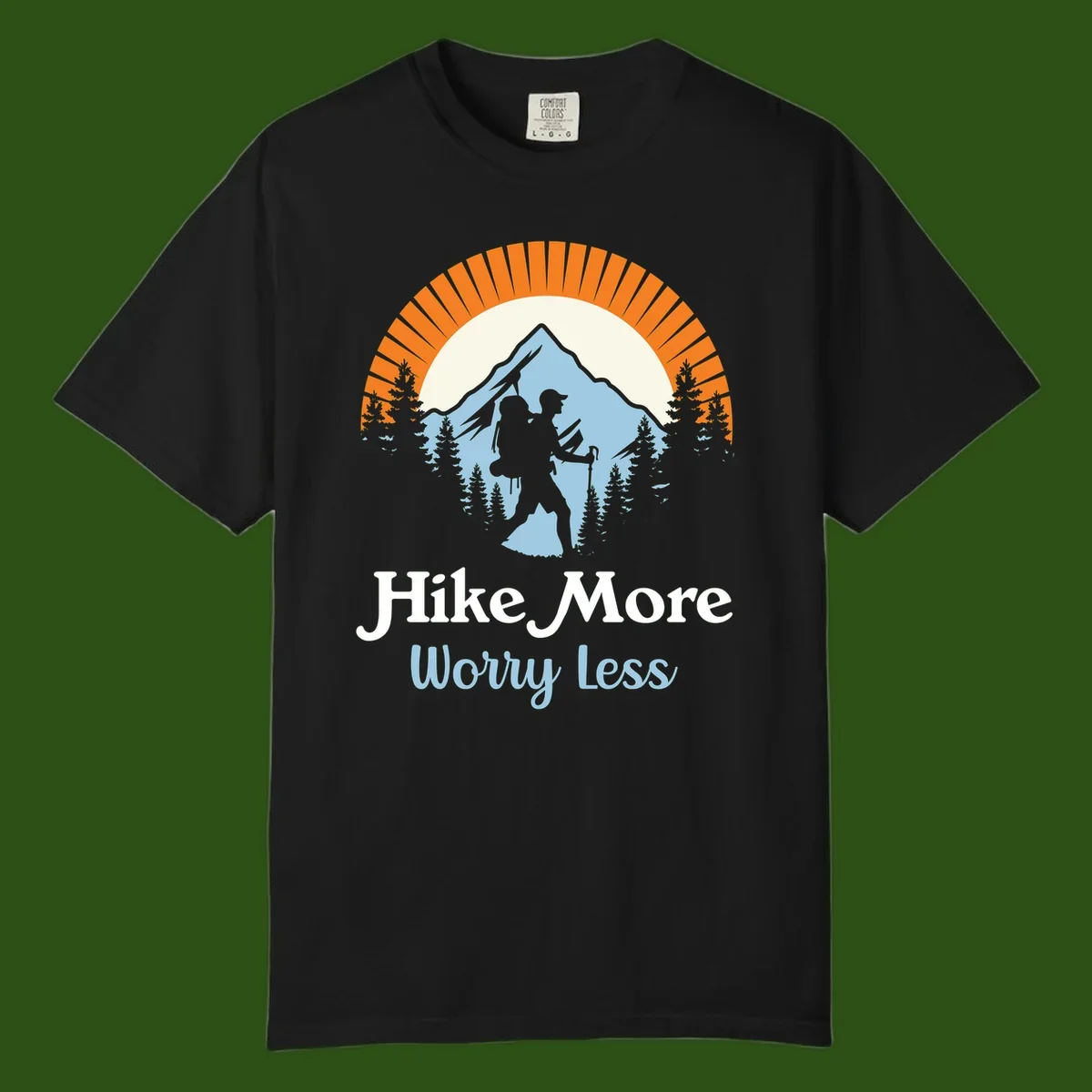 Hike more worry less badge design with silhouetted hiker, mountain peak, and evergreen forest in circular composition.