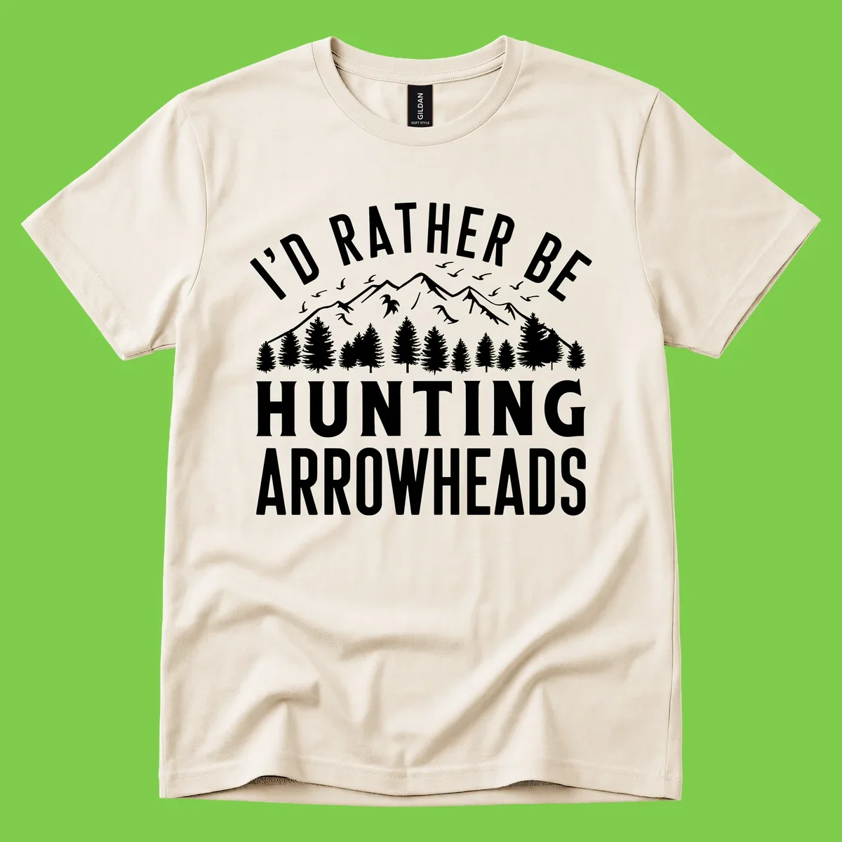 Mountain landscape with evergreen trees and birds, white text reading 'I'd Rather Be Hunting Arrowheads' on gray background