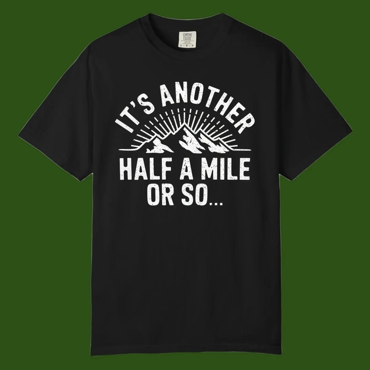 Retro distressed design with mountain peaks and sun rays, text reads 'It's Another Half A Mile Or So' - humorous hiking and camping artwork