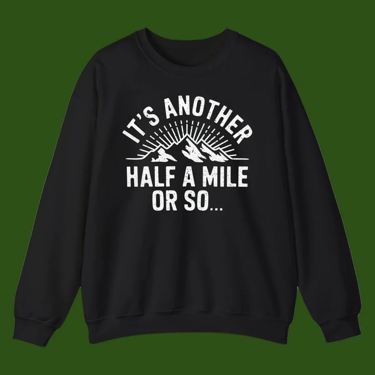 Retro distressed design with mountain peaks and sun rays, text reads 'It's Another Half A Mile Or So' - humorous hiking and camping artwork