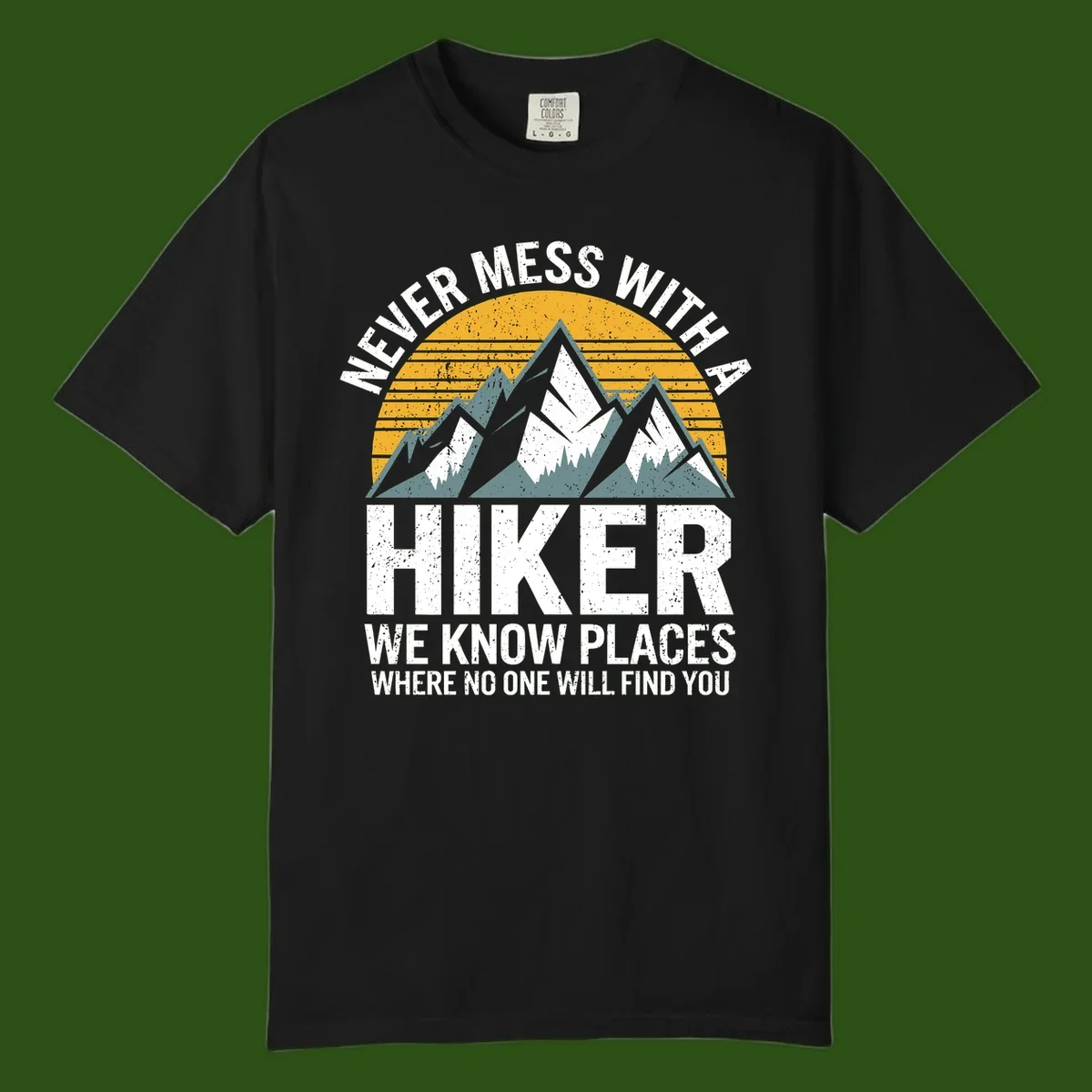 Vintage-style design with snow-capped mountains and forest silhouette against striped sunset, text reads 'Never Mess With A Hiker We Know Places Where No One Will Find You'