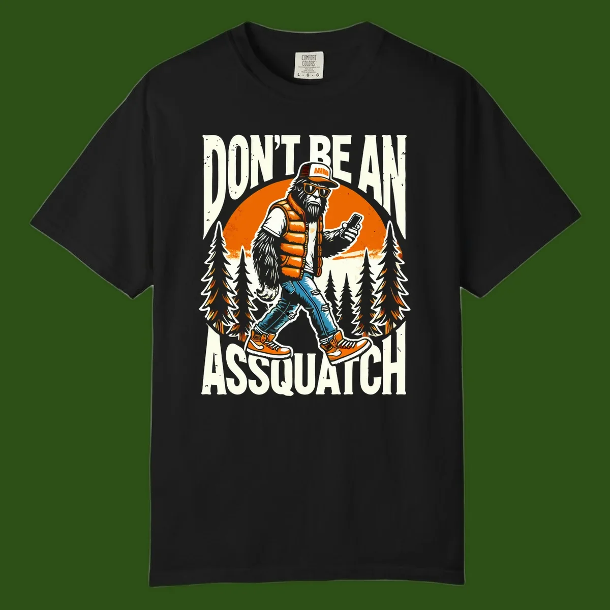 Cartoon sasquatch in hiking gear with backpack and smartphone, 'Don't Be An Assquatch' text, forest and orange sun background.