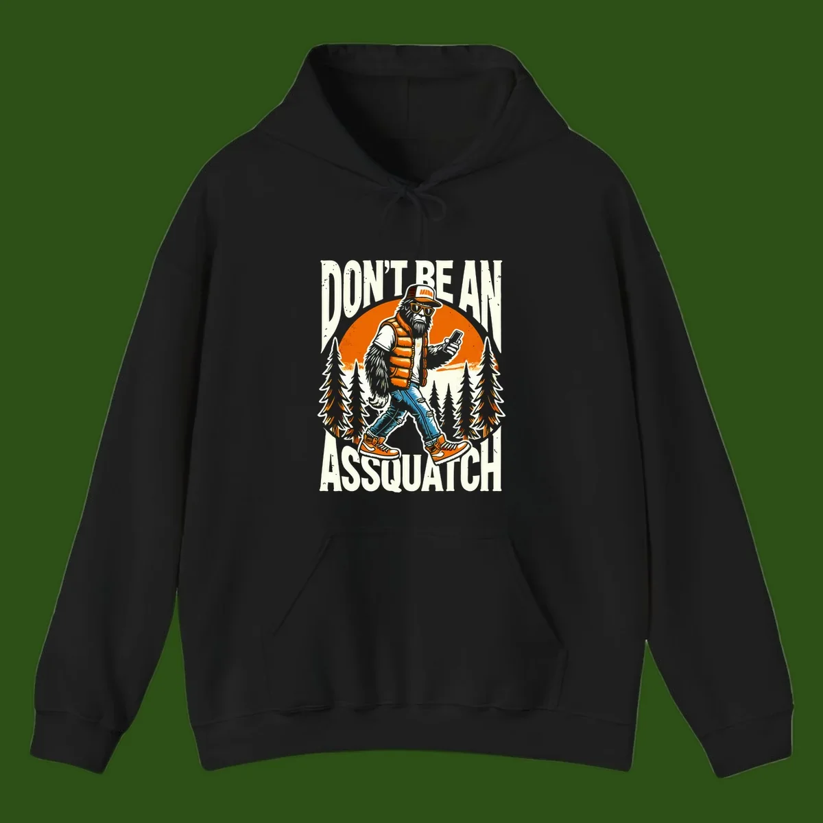 Cartoon sasquatch in hiking gear with backpack and smartphone, 'Don't Be An Assquatch' text, forest and orange sun background.