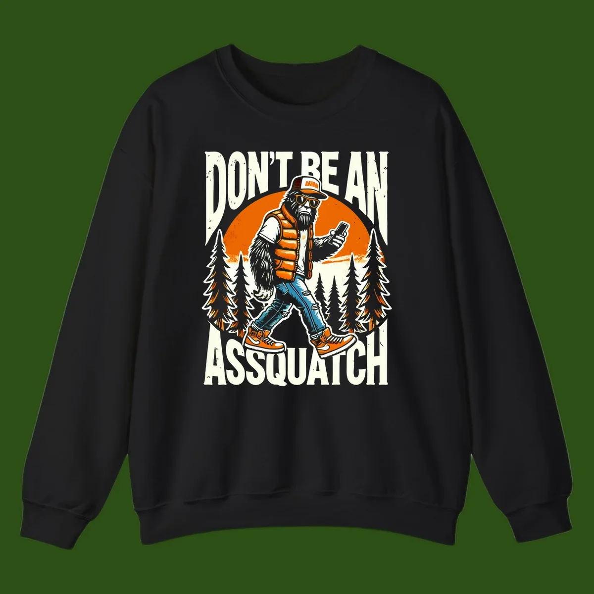 Cartoon sasquatch in hiking gear with backpack and smartphone, 'Don't Be An Assquatch' text, forest and orange sun background.