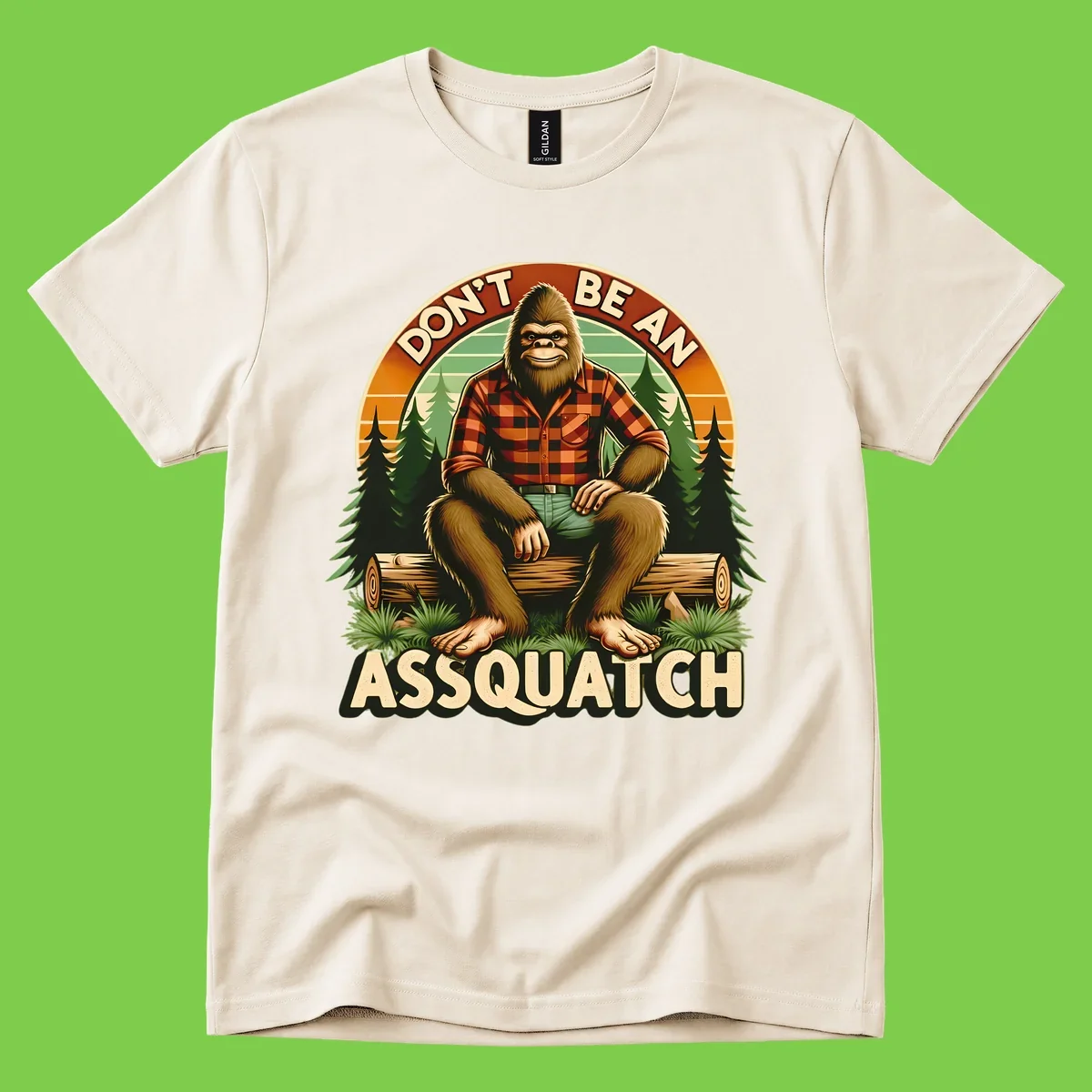 Vintage badge design with friendly Bigfoot in plaid shirt sitting on a log with forest trees, text reads 'Don't Be An Assquatch'
