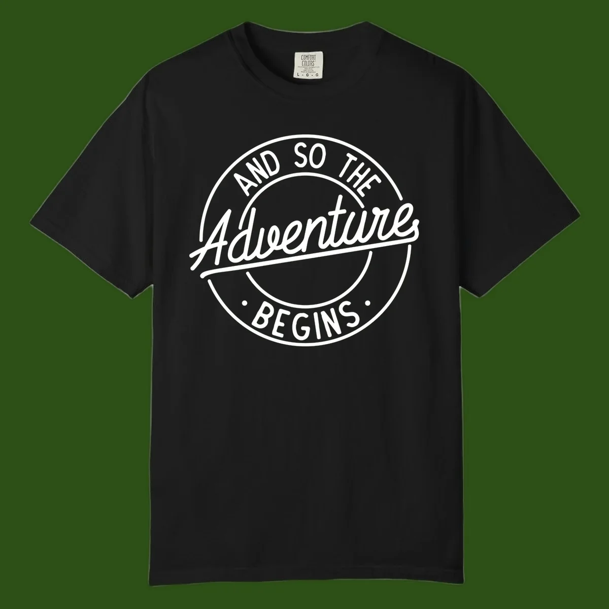 Vintage circular badge design with white text reading 'And So The Adventure Begins' on gray background