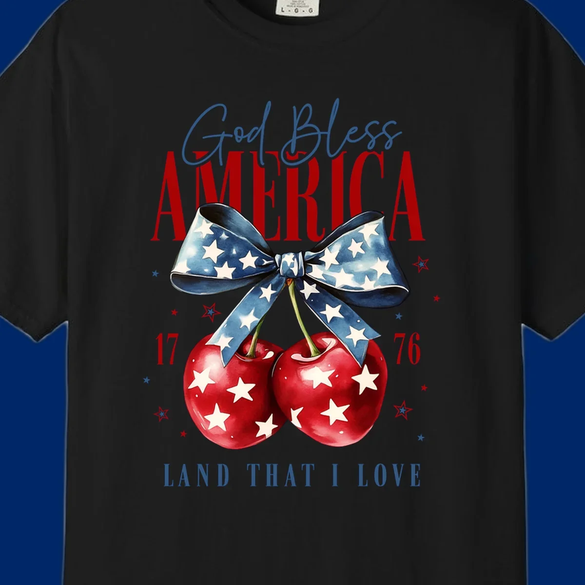 A patriotic design featuring 'God Bless AMERICA' and 'LAND THAT I LOVE' with a blue star-spangled bow, two red star-covered cherries, and the numbers '17' and '76'. god-bless-america-cherries.